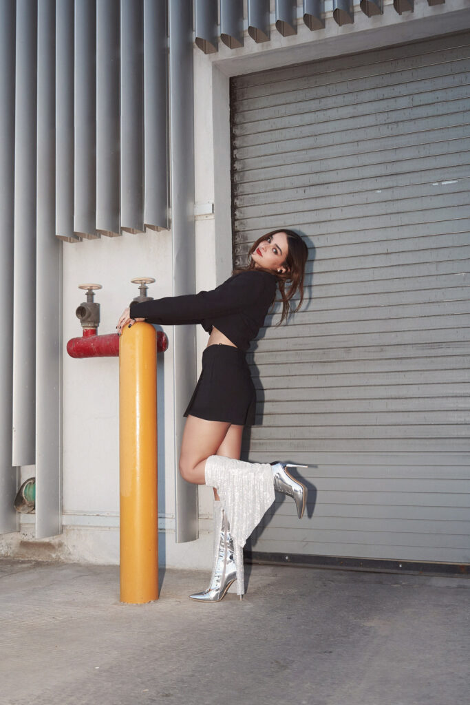 Ana Karina is seen in a dynamic pose wearing sparkling silver boots by Avice